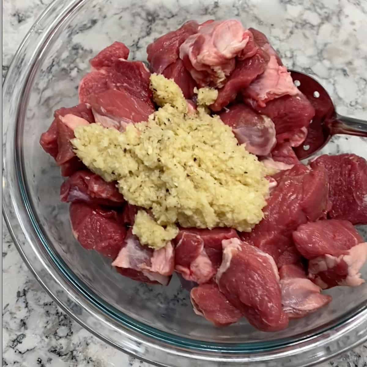 Cubes of lamb in a glass bowl topped with ginger garlic paste