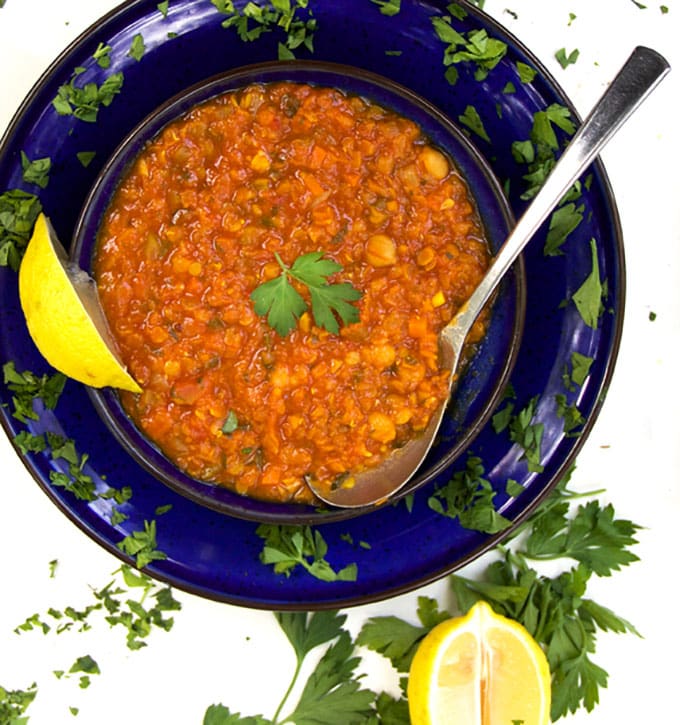 blue bowl filled with red lentil soup with chickpeas, a spoon, a lemon wedge and sprinkles of parsley