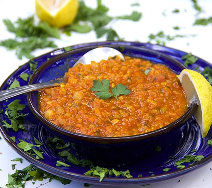 blue bowl with orange lentil soup, a spoon, a lemon and lots of sprinkled parsley