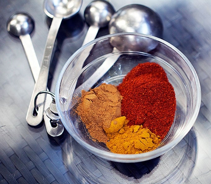 measuring spoons and a glass bowl with three different spices, turmeric, cinnamon and chili powder