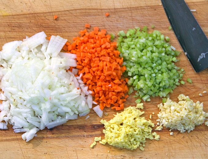 chopped onions, carrots, celery, ginger and garlic on a cutting board with a knife blade