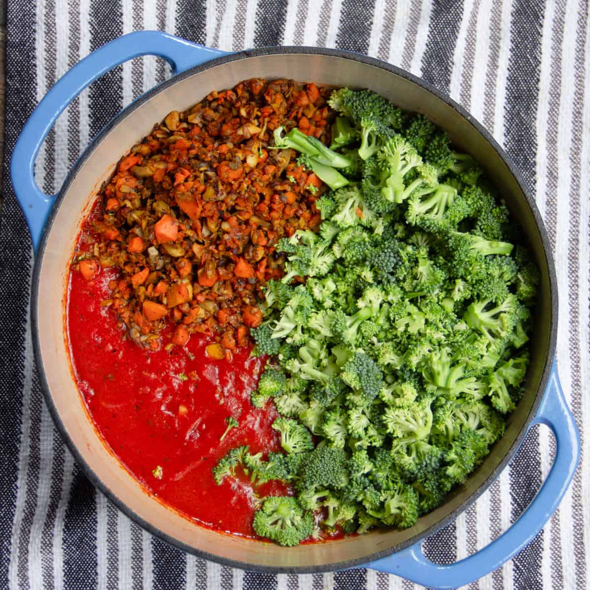 shaved broccoli and caramelized carrot and mushroom sit on top of tomato sauce in a dutch oven.