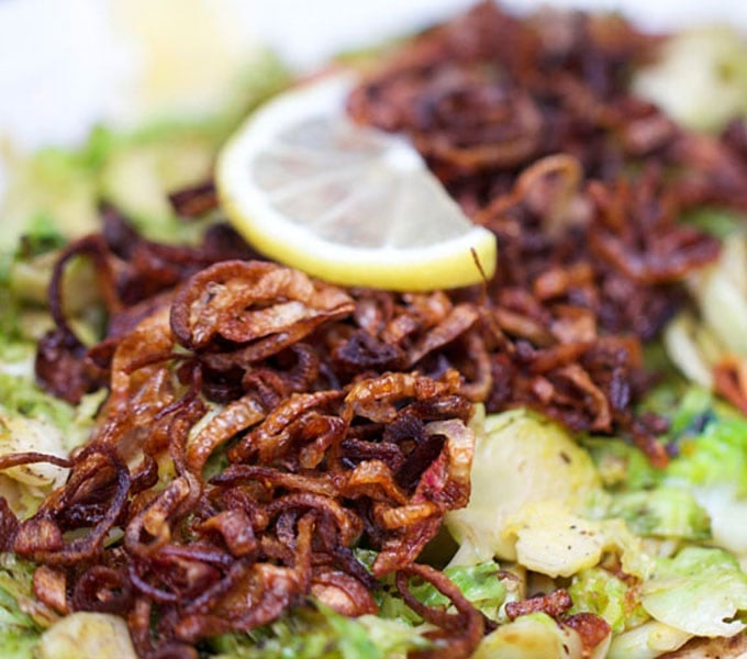 Close up of shredded Brussels Sprouts with Crispy Fried Shallots on top and a small slice of lemon.