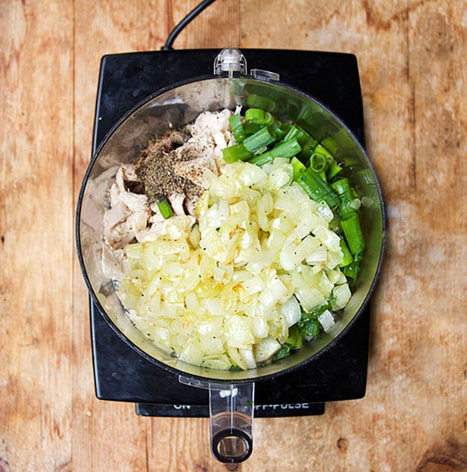 overhead shot of a food processor filled with leftover turkey meat, chopped onions, scallions and spices