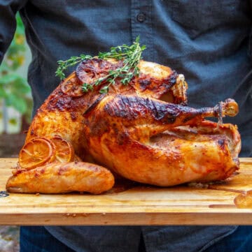 Beautifully golden brown roast turkey on a wooden serving platter, topped with fresh thyme sprigs.