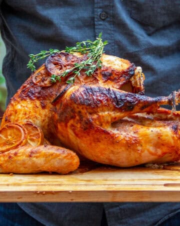 Beautifully golden brown roast turkey on a wooden serving platter, topped with fresh thyme sprigs.