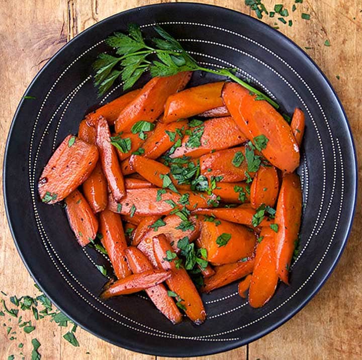 black bowl with glazed carrots and a garnish of chopped parsley