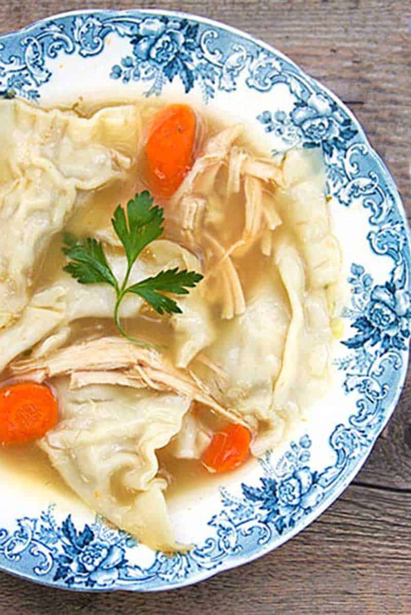 Turkey Soup with turkey dumplings, 3 carrots slices and a sprig of parsley in a blue china bowl