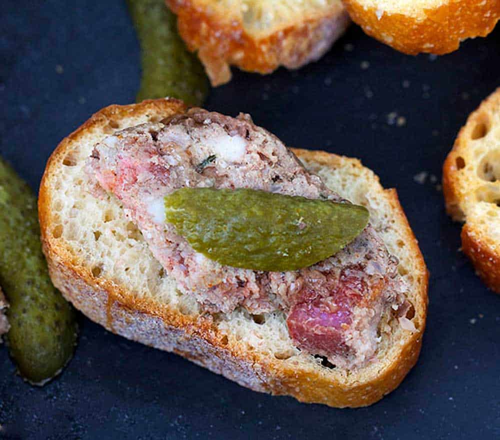 Slice of baguette topped with homemade pate and a sliver of cornichon pickle