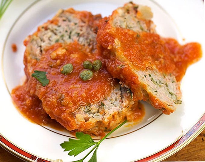 Two slices of Sicilian Turkey Meatloaf with tomato sauce poured over it and a few capers.