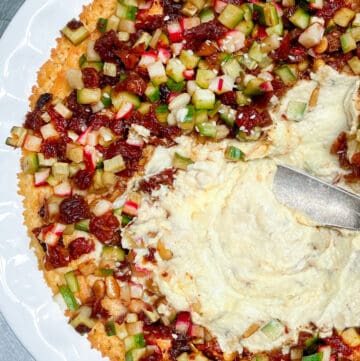 white ceramic pie pan filled with Turkish hummus, topped with chopped cucumbers, radishes and sun dried tomatoes