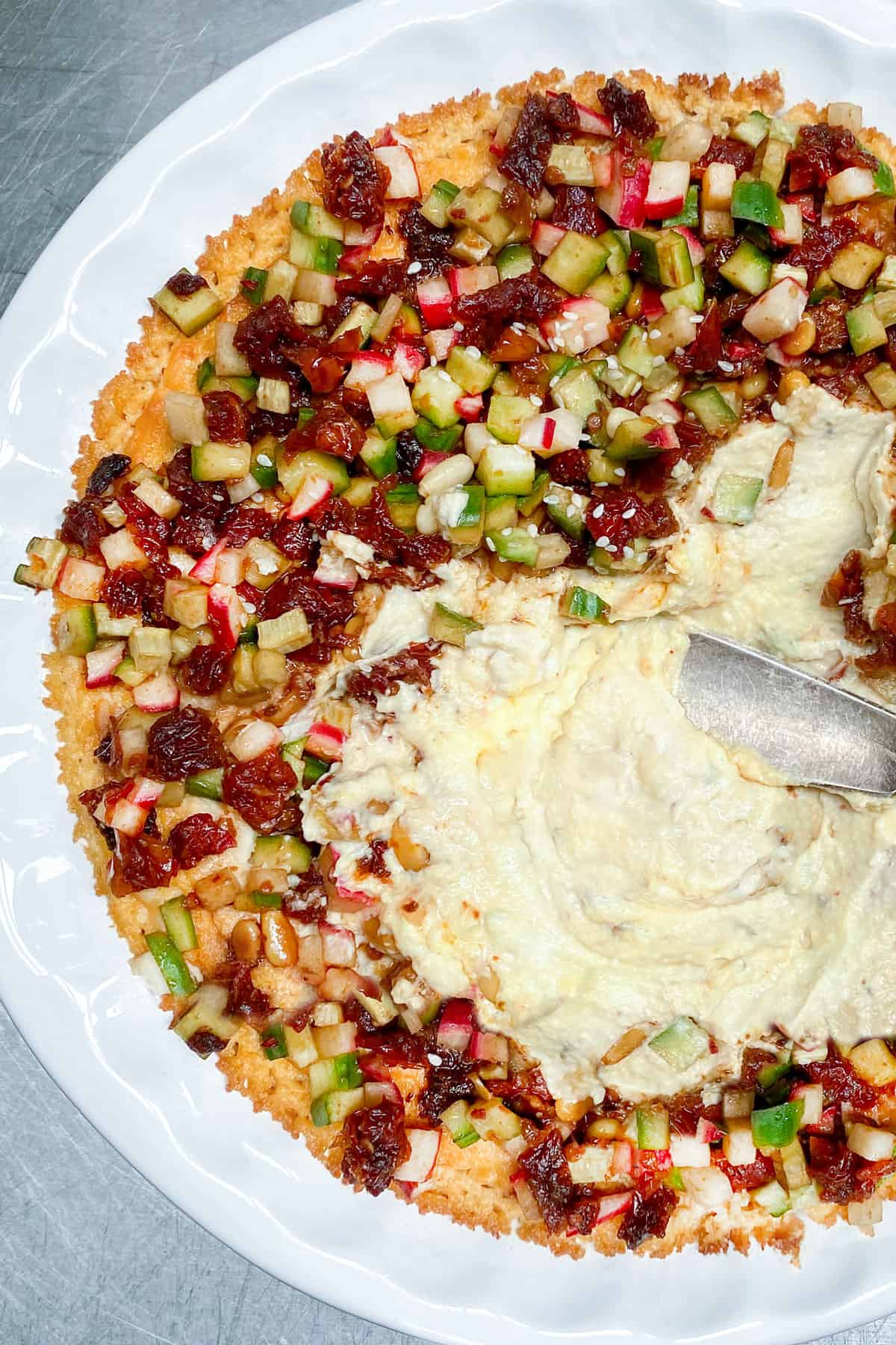 white ceramic pie pan filled with Turkish hummus, topped with chopped cucumbers, radishes and sun dried tomatoes