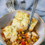 white bowl filled with shepherd's pie and a spoon scooping it up and four forks in the background