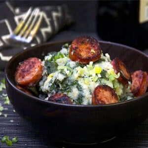 Bowl filled with stamppot: kale mashed potatoes topped with smoky sliced sausages.