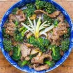 overhead shot showing a blue bowl filled with Chinese beef and broccoli stir fry. A spray of scallions in the center to garnish