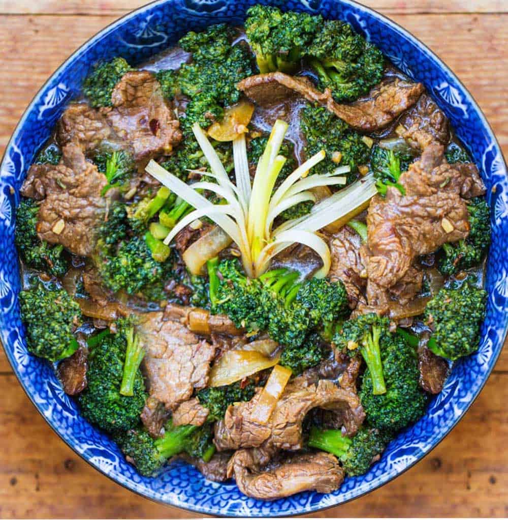 overhead shot showing a blue bowl filled with Chinese beef and broccoli stir fry. A spray of scallions in the center to garnish