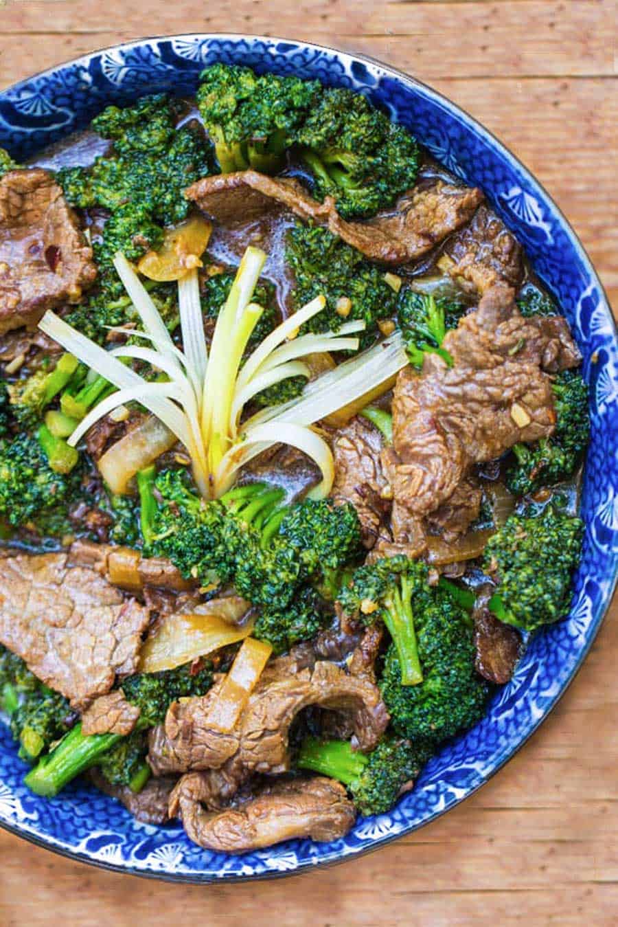  overhead shot showing a blue bowl filled with Chinese beef and broccoli stir fry. A spray of scallions in the center to garnish