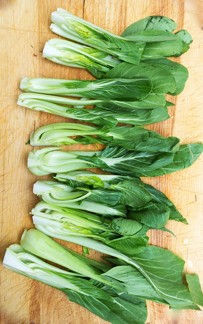 3 heads of baby Bok Choy sliced into ten pieces and set out on a wooden cutting board.