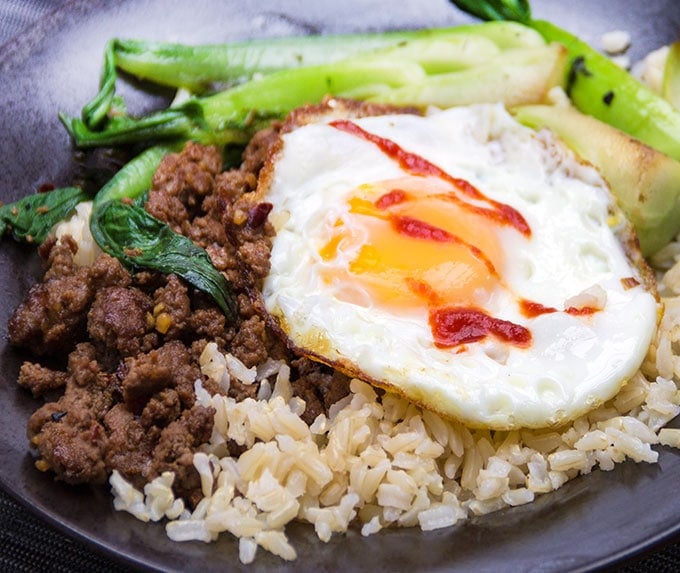 Close up of a Thai Beef Rice Bowl with stir-fried ground beef, brown rice, sautéed bok choy, and a fried egg on top.