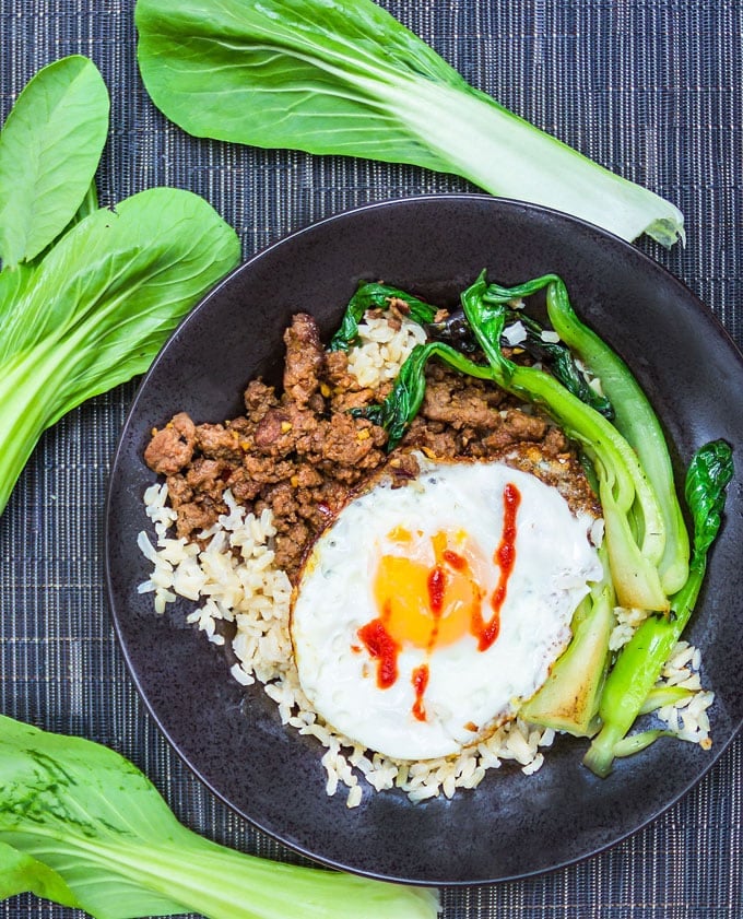 Thai Beef Rice Bowl with sautéed bok choy, a fried egg on top and a zig zag of sriracha hot sauce.