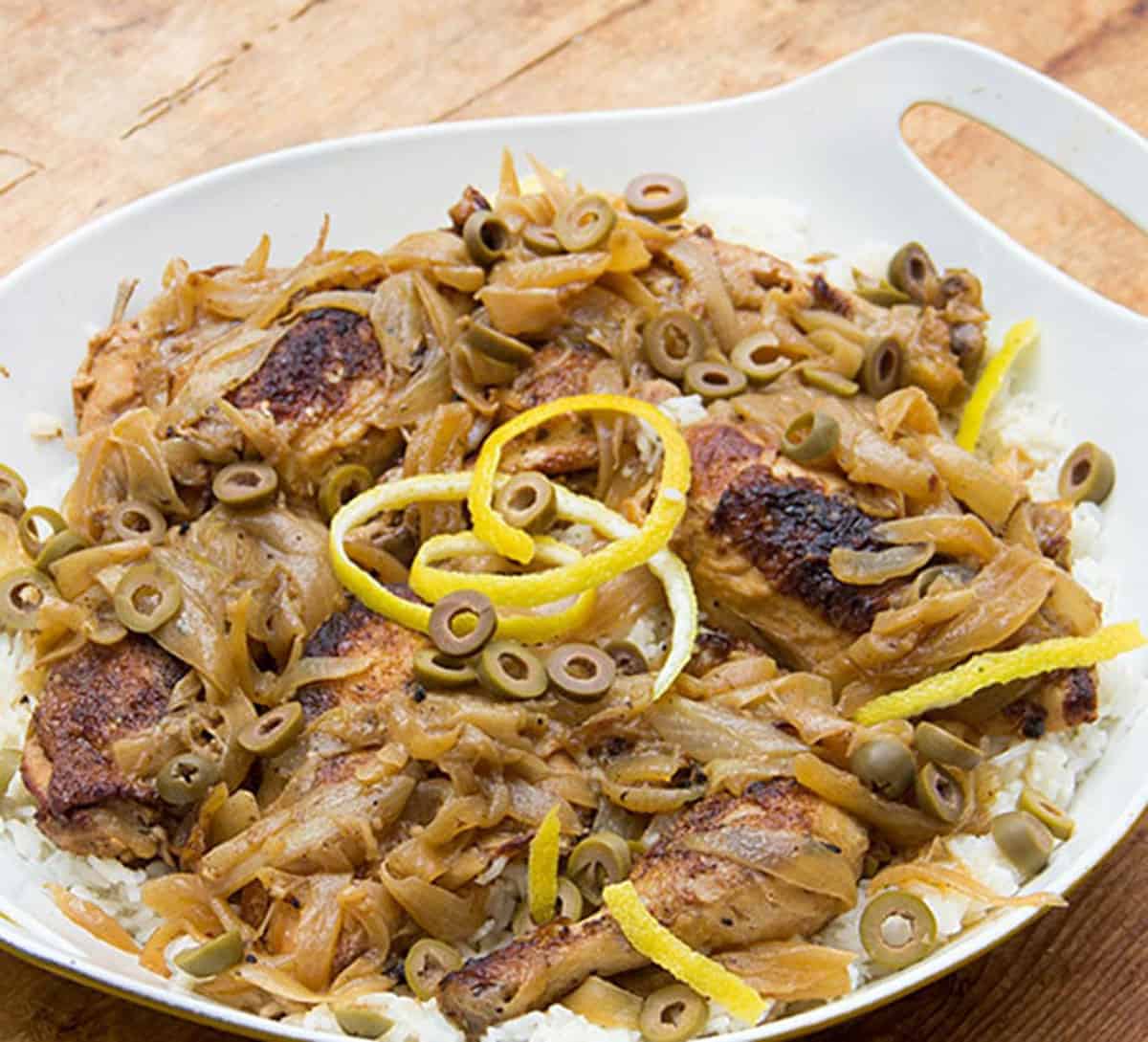 Braised chicken yassa with caramelized onions, olives and decorative lemon zest, in a roasting pan.