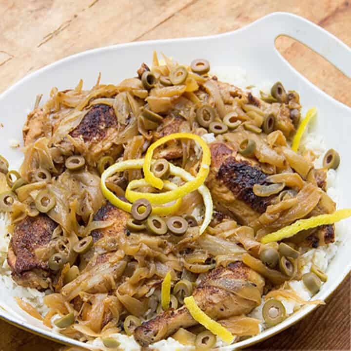 Braised chicken yassa with caramelized onions, olives and decorative lemon zest, in a roasting pan.