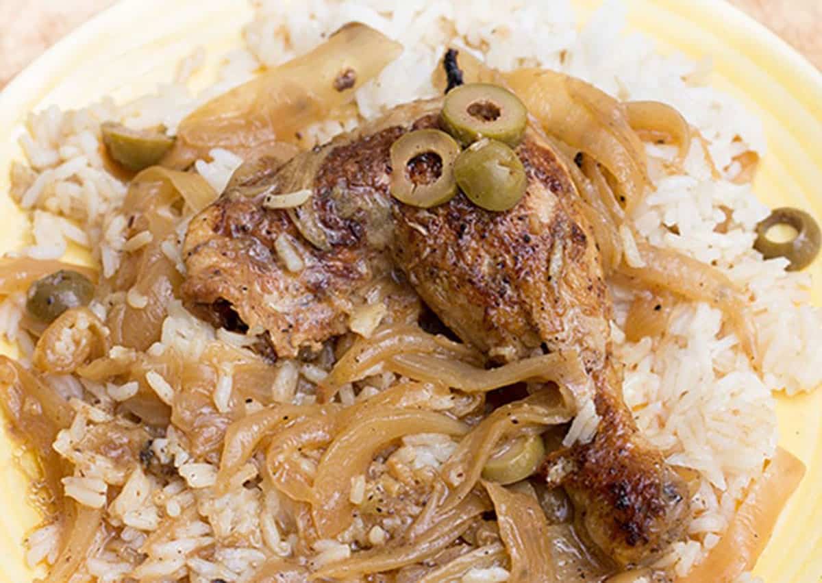 chicken yassa with caramelized onions and sliced olives plated on a bed of rice.