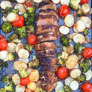 Sheet pan with sliced roasted pork tenderloin arranged down the center, surrounded by roasted potatoes, broccoli and cherry tomatoes.