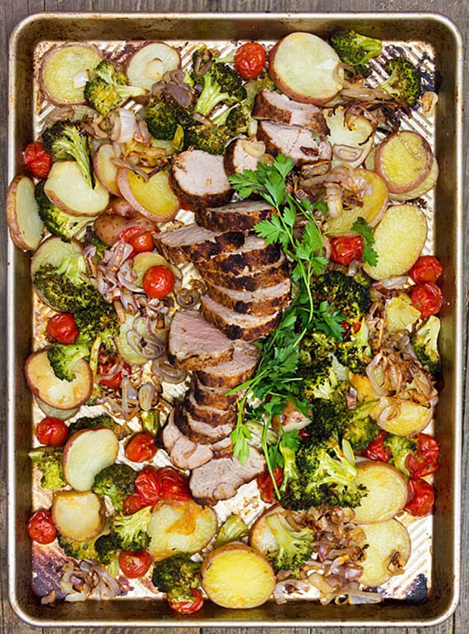 Sheet pan with spice crusted pork, potatoes and vegetables and a garnish of parsley