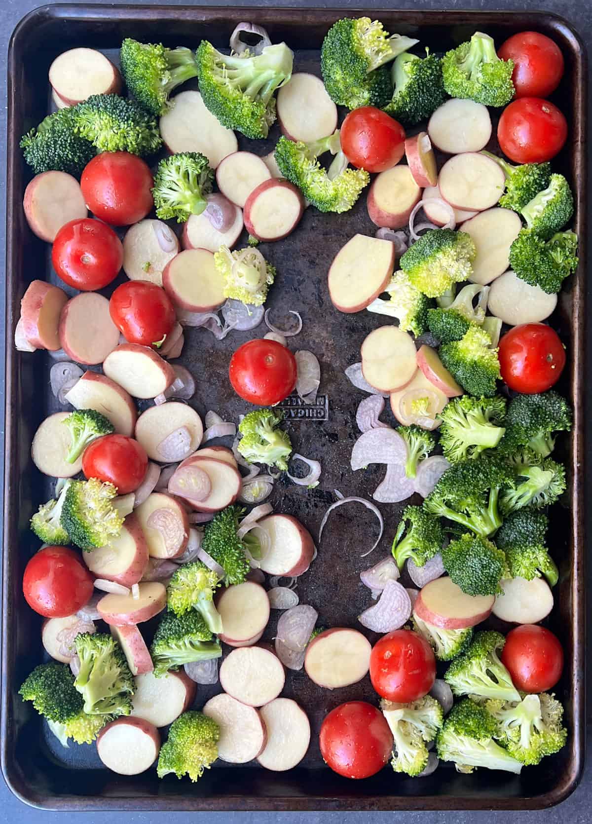 Sheet pan filled with veggies and potatoes, a slit down the center making room for a pork tenderloin.