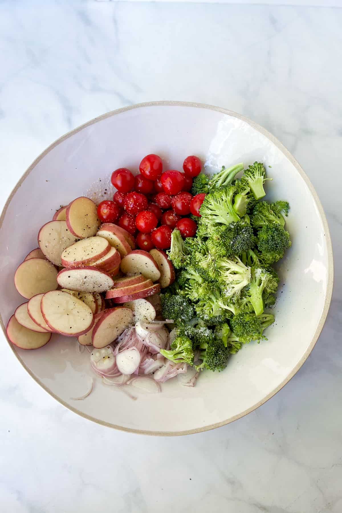 Mixing bowl filled with individual piles of cherry tomatoes, sliced poatoes, broccoli florets and sliced shallots