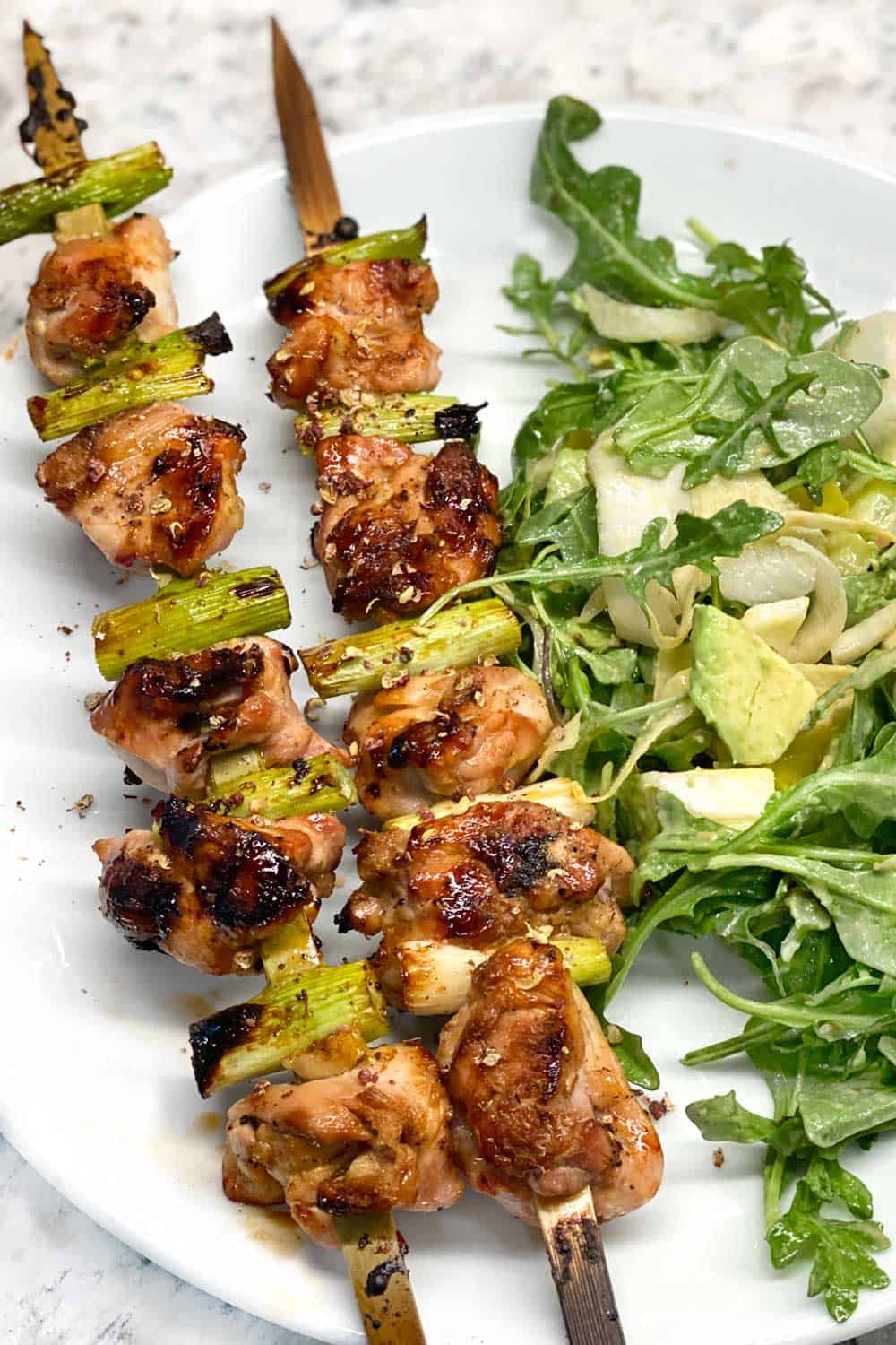 two skewers of chicken yakitori on a white place with salad