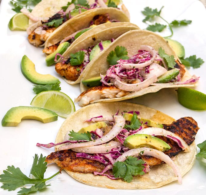 5 fish tacos with red cabbage slaw, sliced avocado, cilantro sprigs and wedges of lime