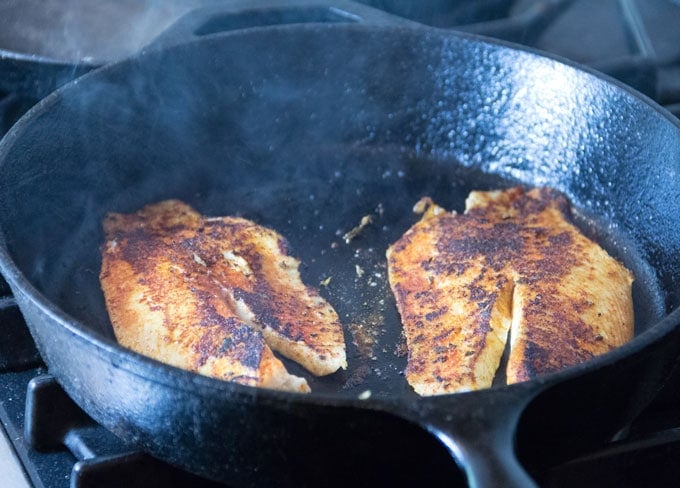 Two blackened fish fillets in a cast iron skillet