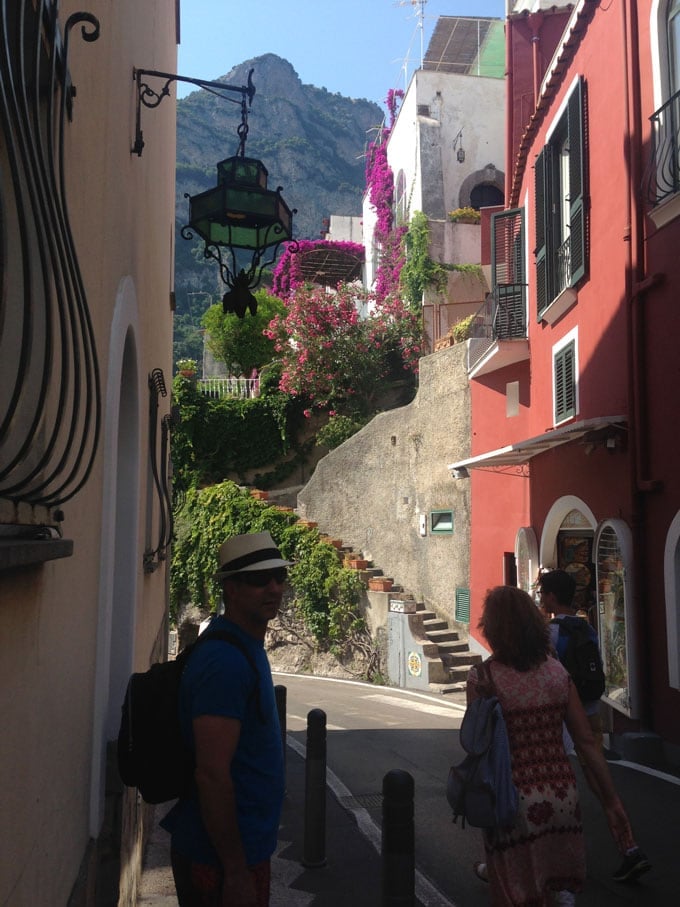 A scene in Positano Italy, looking down a narrow road with colorful buildings and a mountain in the distance.