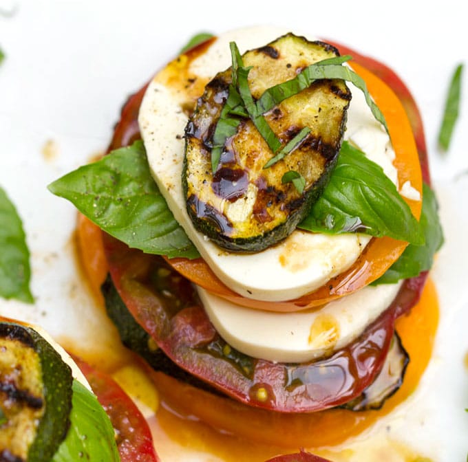 A stacked up caprese salad with layers of tomato, basil, mozzarella and grilled zucchini