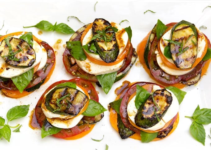 5 zucchini caprese salad stacks on a white platter with sprigs of basil strewn around