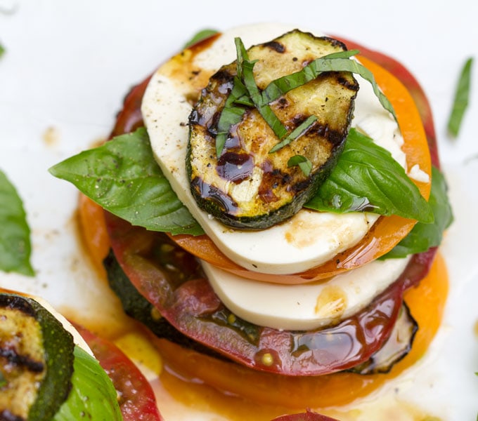 One stack of Grilled Zucchini Caprese Salad with layers of sliced tomatoes, mozzarella cheese, grilled zucchini rounds and basil leaves