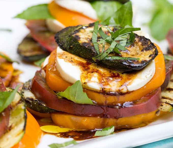 A close up of a grilled zucchini caprese salad stack with drizzles of olive oil and balsamic and slivered basil on top