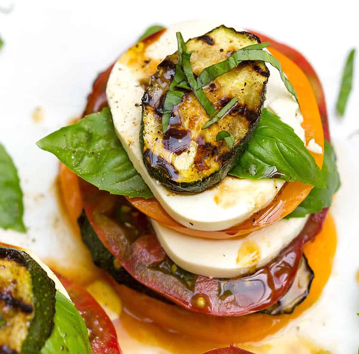 caprese salad stacks with layers of tomato, mozzarella and grilled zucchini and basil leaves.
