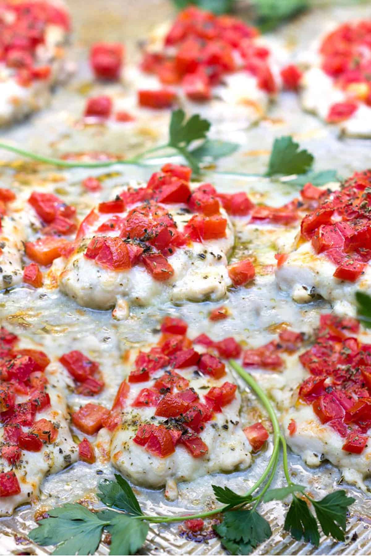 Baked chicken fillets topped with chopped tomatoes on a sheet pan