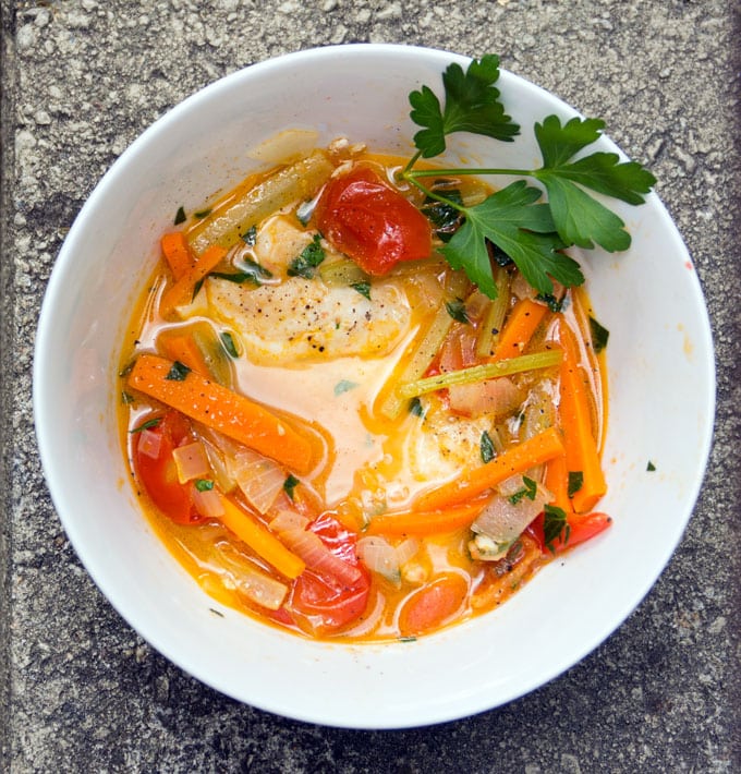 White bowl filled with poached fish and vegetables