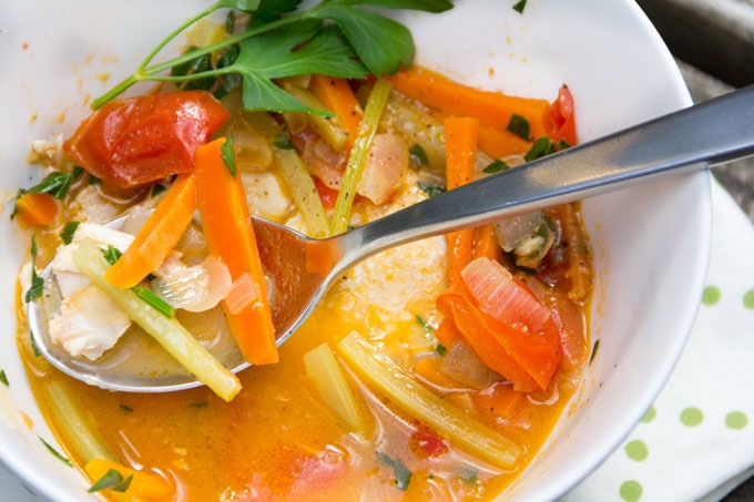 Close up of a bowl and a spoon with fish, carrots, celery and tomatoes and broth 