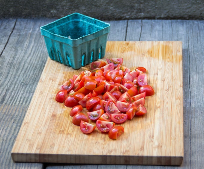 wooden cutting board with empty pint container and a pile of quartered cherry tomatoes