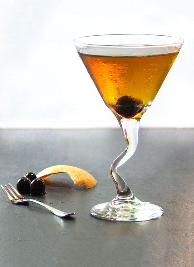 A martini glass with a perfect manhattan and cherries and orange zest