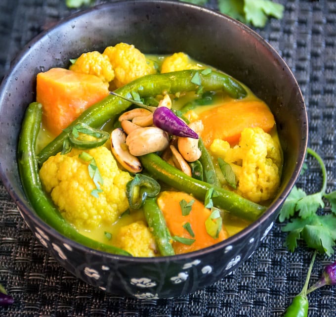 Sri Lankan Vegetable Curried vegetables, sweet potatoes, green beans and cauliflower, in a black bowl with cilantro and toasted cashews