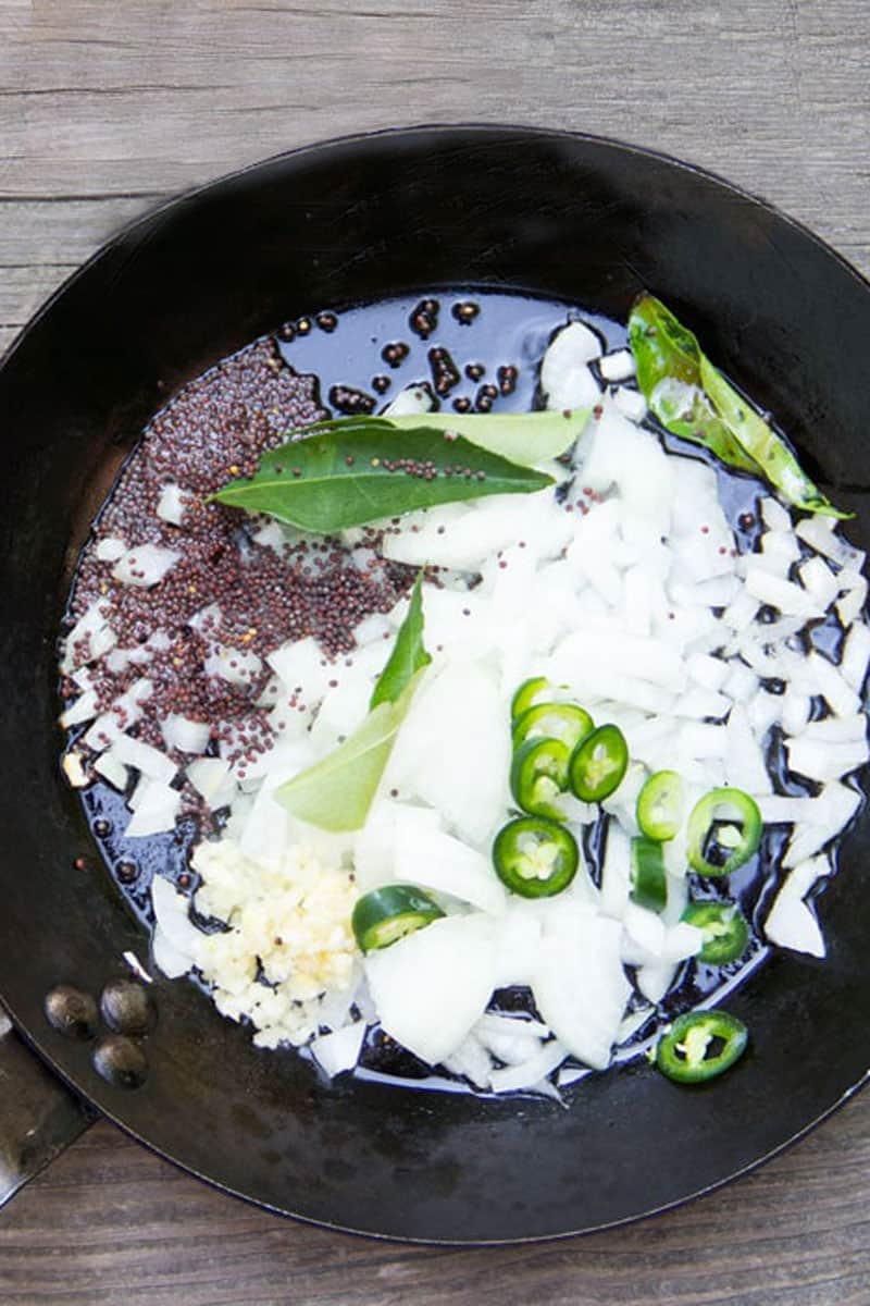 chopped onions, minced garlic, sliced jalapenos and black mustard seeds sautéeing in a black frying pan