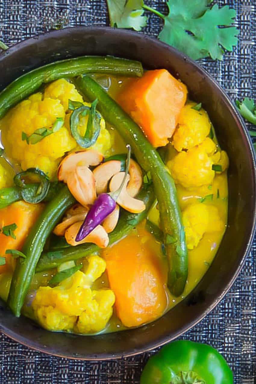 black bowl filled with colorful vegetable curry of cauliflower, sweet potatoes and green beans