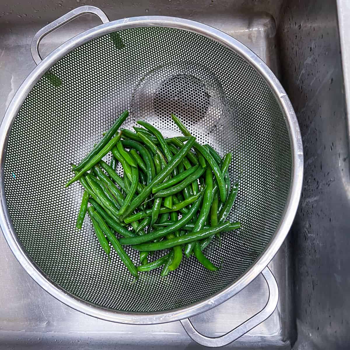 blanched green beans draining in a colander in the sink.
