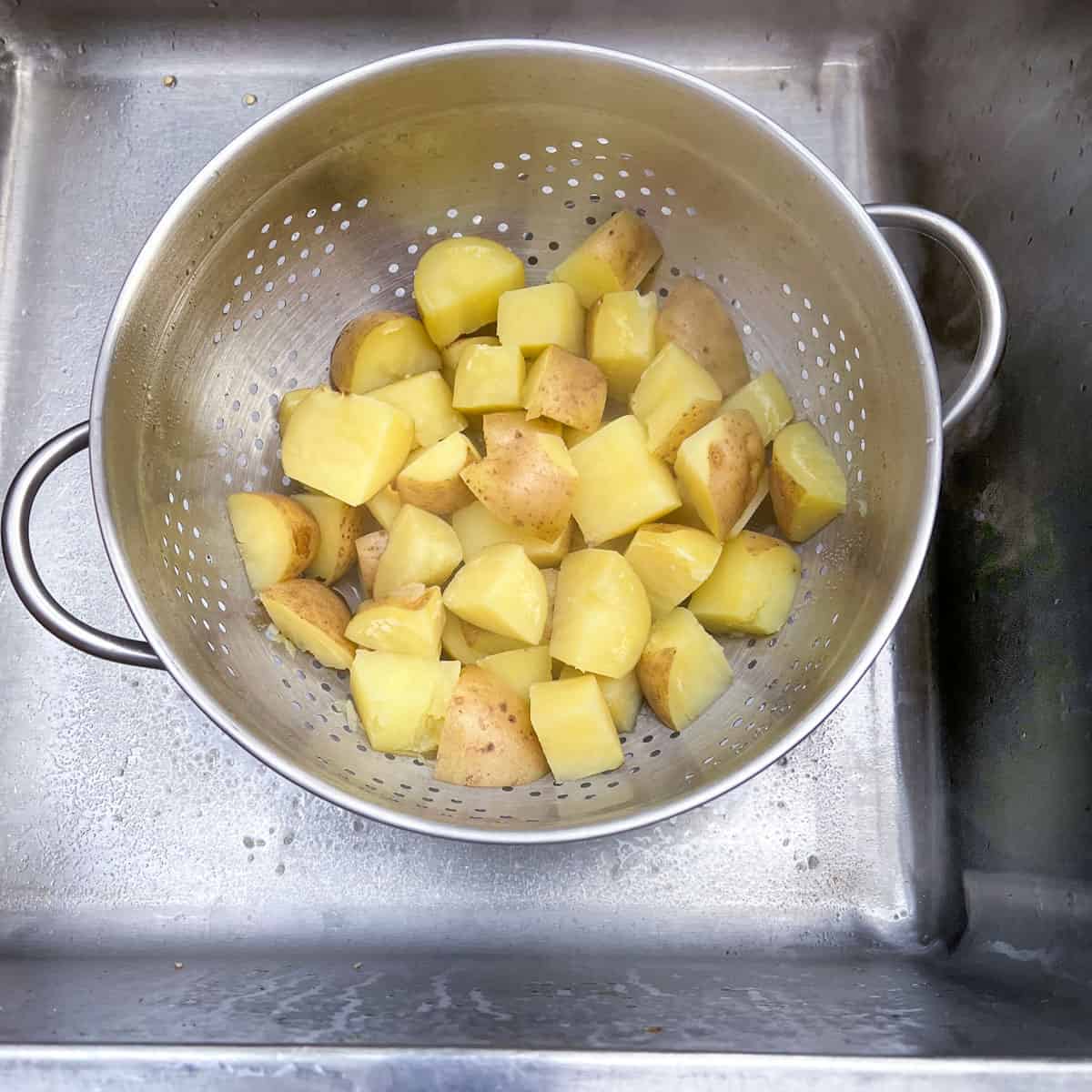 chunks of boiled potatoes draining in a colander in the sink.